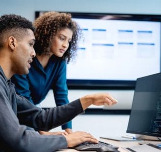 Two software professionals working together on a laptop beside a digital display
