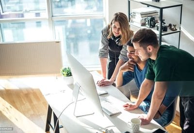 Technology professionals collaborating around a desktop computer in an office