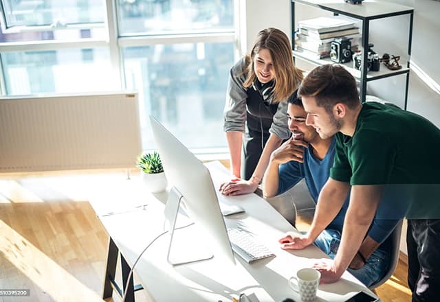 Technology professionals collaborating around a desktop computer in an office
