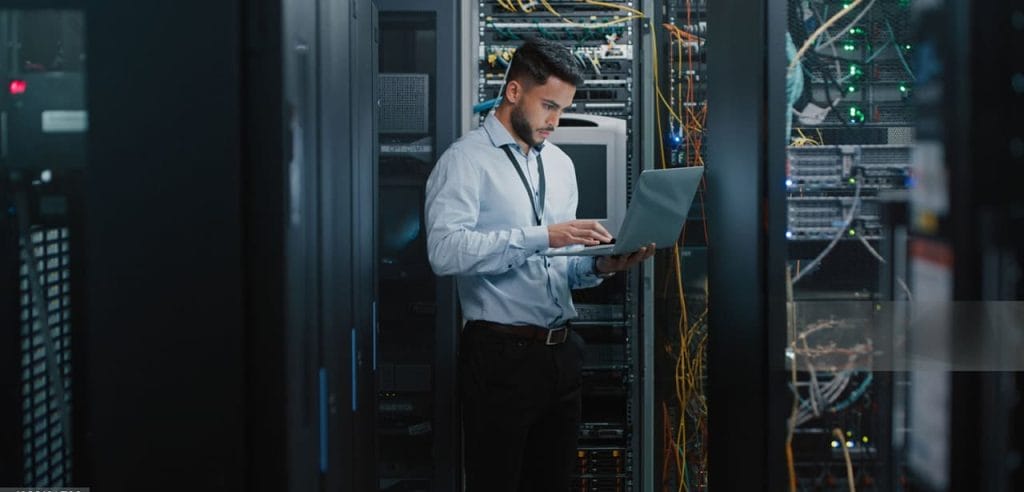 IT specialist working on a laptop beside network servers in a data centre